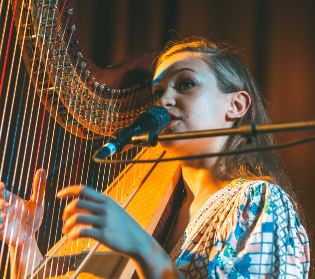 Joanna Newsom singing at her harp under warm stage light